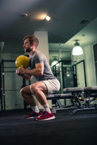 53242676 - man doing squats with kettlebell in gym.
